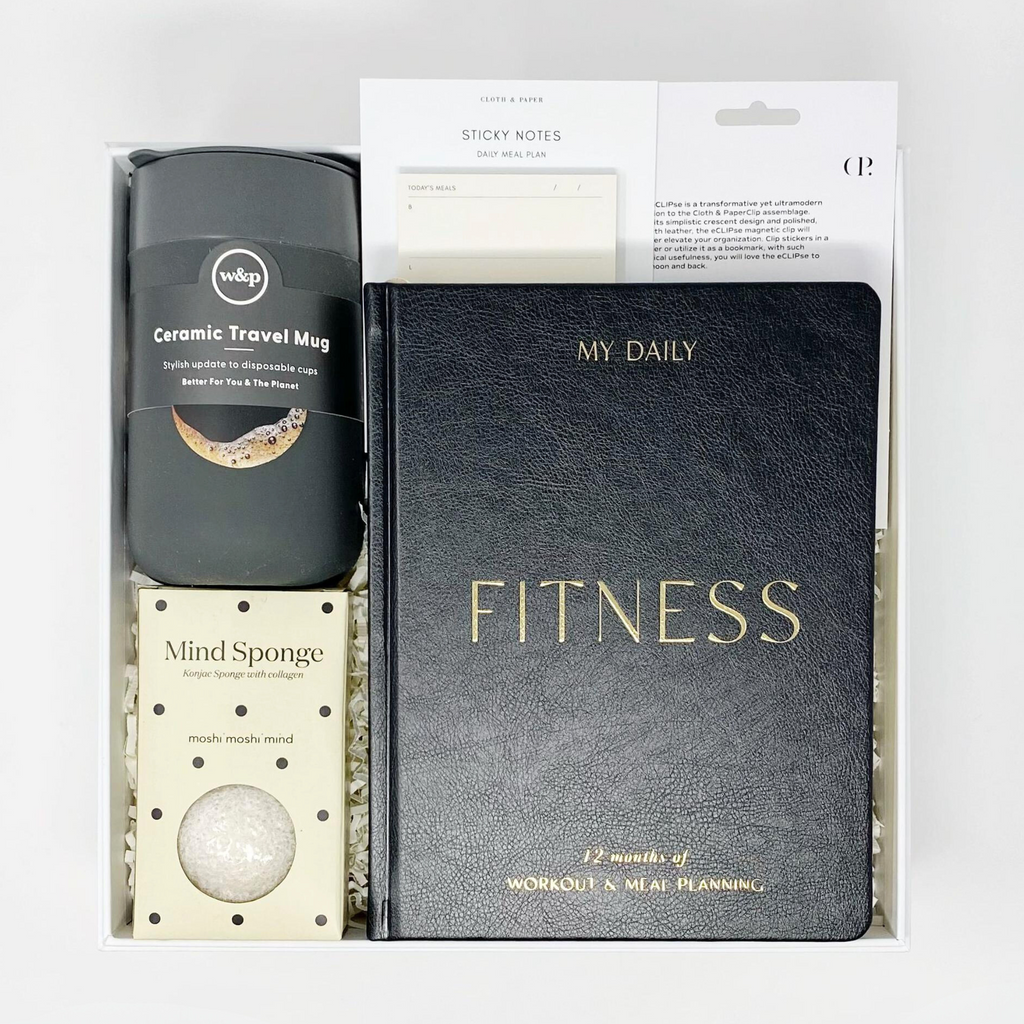 Fitness focused gift box. Contents include a W&P Ceramic Travel Mug, Moshi Moshi Mind Mind Sponge, Blush & Gold Daily Fitness Planner, Cloth & Paper Daily Meal Plan Sticky Notes, and Cloth & Paper eCLIPse Bookmark. Gift box made from recycled materials